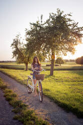 Teenager-Mädchen steht neben Fahrrad auf unbefestigten Weg bei Sonnenuntergang - LVF08167