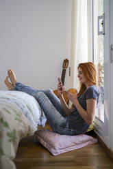 Junge Frau zu Hause, die im Schlafzimmer chillt und ihr Smartphone benutzt - AFVF03579