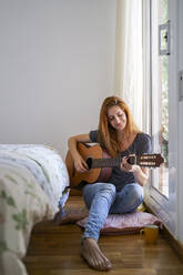 Junge Frau zu Hause im Schlafzimmer chillen und Gitarre spielen - AFVF03582