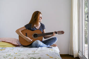 Junge Frau zu Hause im Schlafzimmer chillen und Gitarre spielen - AFVF03591