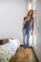 Junge Frau zu Hause, die im Schlafzimmer chillt und ihr Smartphone benutzt - AFVF03593