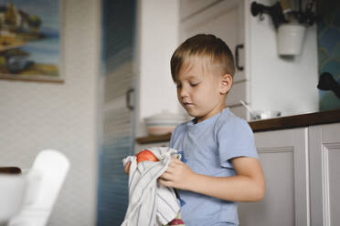 Porträt eines kleinen Jungen, der einen Pfirsich mit einem Küchenhandtuch trocknet - EYAF00296