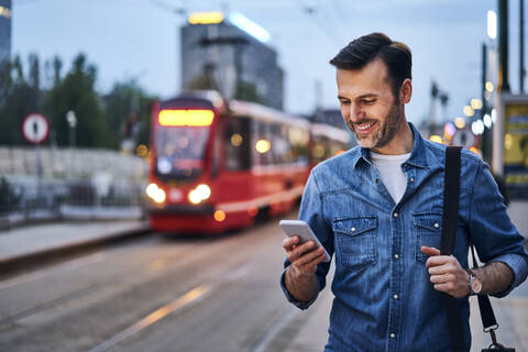 Man using smartphone while waiting for public tram in the evening stock photo