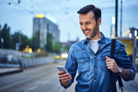 Mann steht mit Smartphone und wartet auf den Feierabendverkehr, lizenzfreies Stockfoto