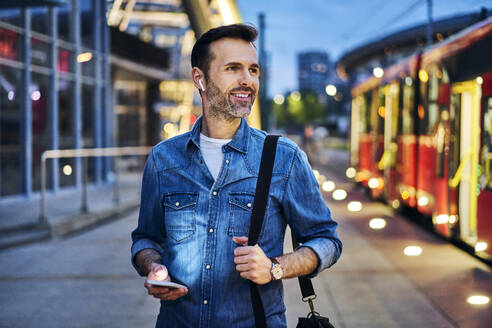 Mann hört Musik beim Warten auf die Straßenbahn während des abendlichen Pendelns nach der Arbeit - BSZF01089