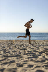 Barechested man jogging on the beach - MAUF02668