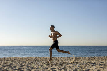 Mann mit nacktem Oberkörper beim Joggen am Strand - MAUF02669