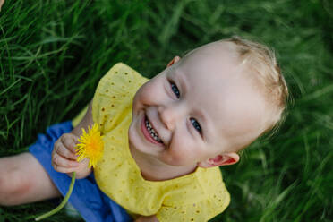 Portrait of happy little girl with dandelion sitting on a meadow - OGF00030