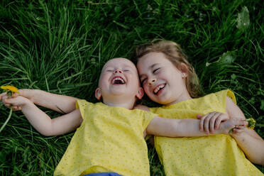 Zwei lachende Schwestern liegen auf einer Wiese und tragen gelbe Oberteile - OGF00031