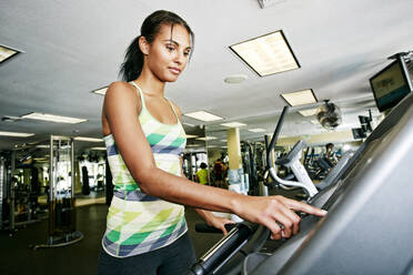 Mixed race woman using treadmill in gymnasium - BLEF09493