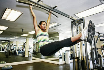 Mixed race woman doing pull-ups in gymnasium - BLEF09499