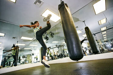 Mixed race woman kicking punching bag in gymnasium - BLEF09504