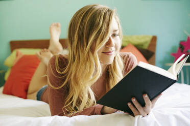 Caucasian woman reading book on bed - BLEF09548