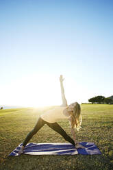 Kaukasische Frau übt Yoga auf einem Feld - BLEF09557