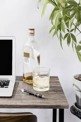 Whisky auf dem Schreibtisch neben dem Laptop im Büro - FSIF03954