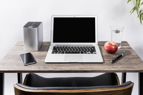 Laptop, Smartphone, Apfel, Wasser und Stift auf dem Schreibtisch - FSIF03960
