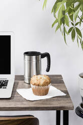 Isolierter Kaffeebecher und Muffin auf dem Schreibtisch neben dem Laptop im Büro - FSIF03997