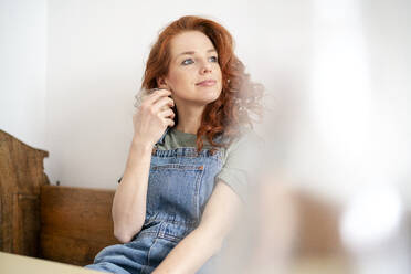 Thoughtful redhead woman holding drink while looking away at home - DMOF00153