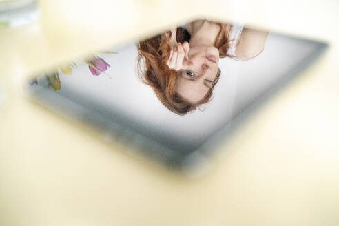 Spiegelung einer Frau auf einem digitalen Tablet über einem Tisch zu Hause - DMOF00165
