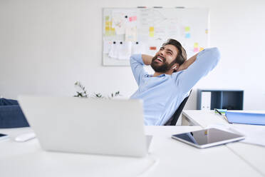 Laughing businessman sitting at a desk - BSZF01132