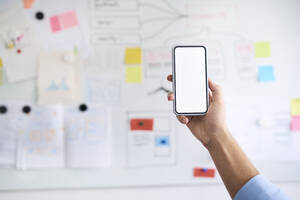 Male hand holding aloft a smartphone in front of a whiteboard - BSZF01139