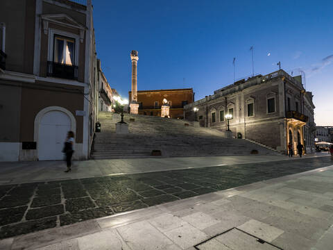 Beleuchtete römische Säule auf Stufen inmitten von Gebäuden in Brindisi gegen den Nachthimmel, lizenzfreies Stockfoto