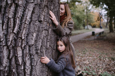 Portrait of little girl hugging tree with her mother - OGF00042