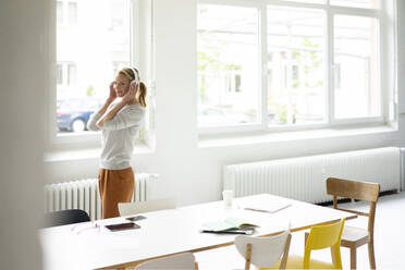 Junge Geschäftsfrau, die im Büro mit Kopfhörern Musik hört - JOSF03458