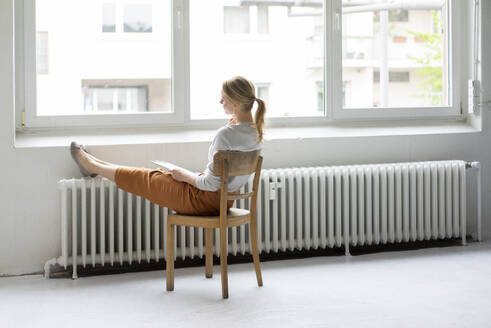 Junge Frau sitzt auf einem Stuhl am Fenster im Büro - JOSF03460