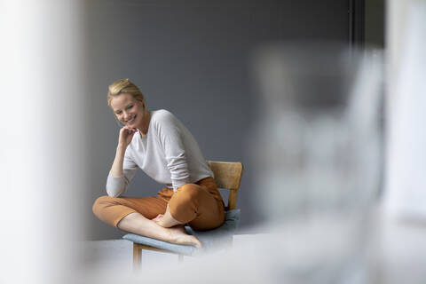 Lächelnde junge Frau sitzt auf einem Stuhl im Büro, lizenzfreies Stockfoto