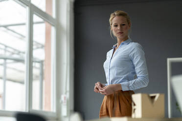 Ernste junge Frau im Büro mit Architekturmodell auf dem Schreibtisch - JOSF03482