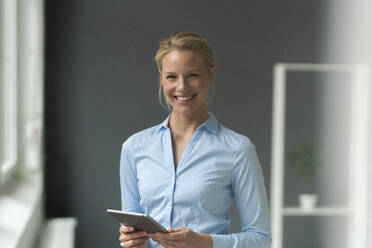 Portrait of smiling young businesswoman with tablet in office - JOSF03491