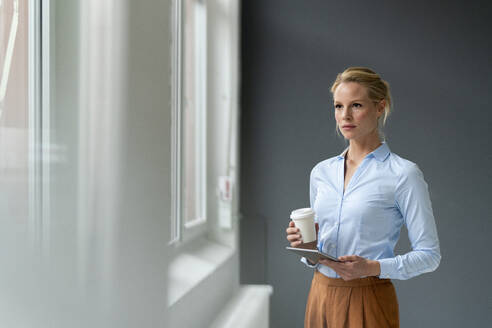 Thoughtful young businesswoman with tablet and takeaway coffee in office - JOSF03494