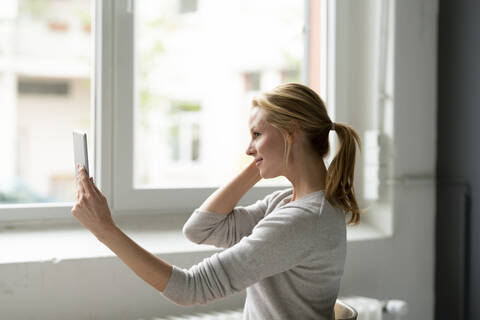 Lächelnde junge Frau mit Tablet am Fenster, lizenzfreies Stockfoto