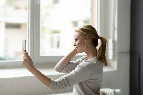 Lächelnde junge Frau mit Tablet am Fenster - JOSF03510