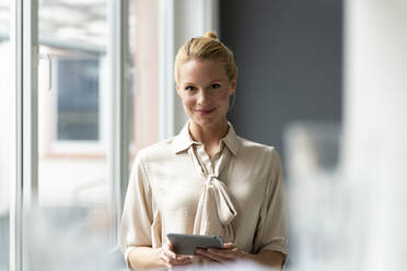 Portrait of smiling young businesswoman with tablet at the window - JOSF03524