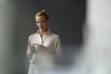 Porträt einer lächelnden jungen Geschäftsfrau mit einer Tasse Kaffee - JOSF03529