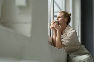 Junge Geschäftsfrau mit einer Tasse Kaffee und Blick aus dem Fenster - JOSF03532