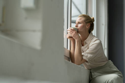 Young businesswoman with cup of coffee looking out of window - JOSF03532