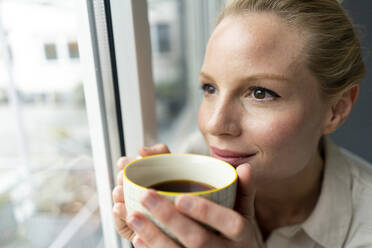 Young businesswoman with cup of coffee looking out of window - JOSF03534