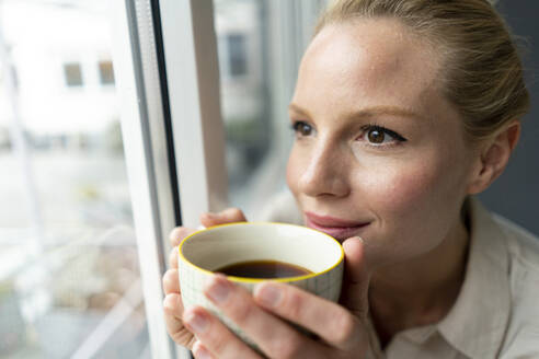 Junge Geschäftsfrau mit einer Tasse Kaffee und Blick aus dem Fenster - JOSF03534