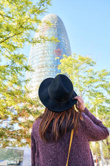 Rückenansicht einer Frau mit Hut und Blick auf den Torre Glories, Barcelona, Spanien - GEMF02991