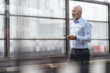 Mature businessman with cell phone at the station platform - DIGF07383