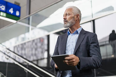 Mature businessman with tablet looking around - DIGF07393