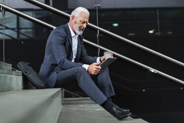 Älterer Geschäftsmann sitzt auf einer Treppe und benutzt ein Tablet - DIGF07412