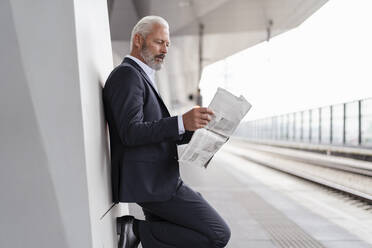 Älterer Geschäftsmann, der auf dem Bahnsteig Zeitung liest - DIGF07430