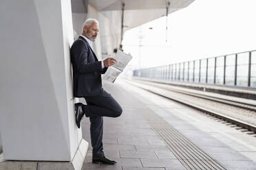 Älterer Geschäftsmann, der auf dem Bahnsteig Zeitung liest - DIGF07431