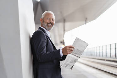 Glücklicher reifer Geschäftsmann mit Zeitung auf dem Bahnsteig - DIGF07432