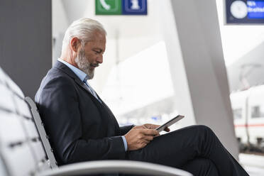 Älterer Geschäftsmann sitzt im Wartebereich und benutzt ein Tablet - DIGF07458