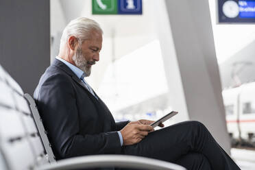 Mature businessman sitting in waiting area using tablet - DIGF07458